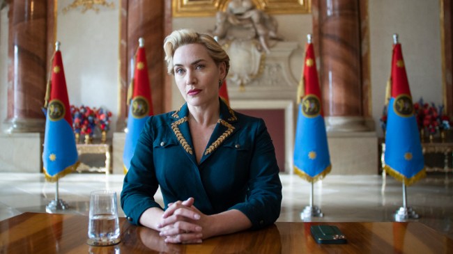 Kate Winslet dans le rôle d'Elena Vernham est assise à une table avec une rangée de drapeaux derrière elle dans le film 